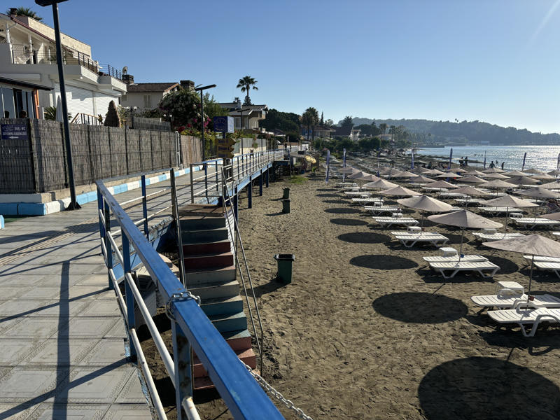 Resim 5. Arsuz Belediyesi’nin 2016’nın yaz aylarında tamamladığı sahil yürüme yolunun özel villaların önünden geçen kısmı. Villaların önü kamış perdelerle kapatılmış. Plaja inen çelik merdivenin kötü işçiliği ise basamakların renkli boyasıyla, korkulukların pası ise Akdeniz’in sert güneşi altında hoş görülebilir küçük kusurlar hale gelmiş. 